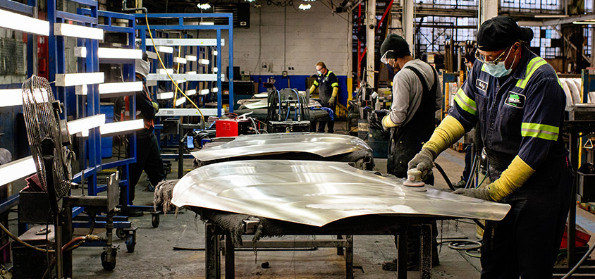 Three men working within an aisle of the New Center facility. Smoothing down silver sheets of metal