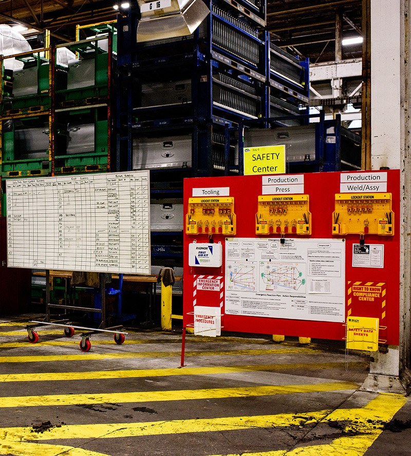 Whiteboard on the left with multiple columns and rows with checks and various notes. On the right, a large red board with the title Safety Center. Whiteboard on the left with multiple columns and rows with checks and various notes. On the right, a large red board with the title Safety Center.